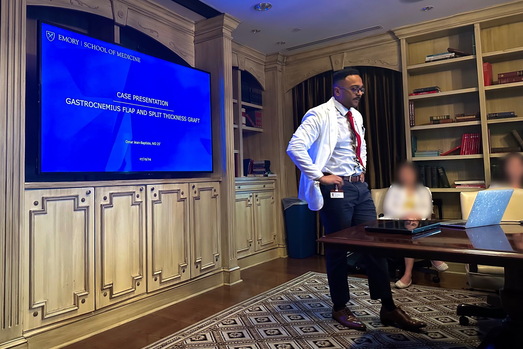 Omar Jean-Baptiste presenting in a meeting room, with the other attendees blurred.